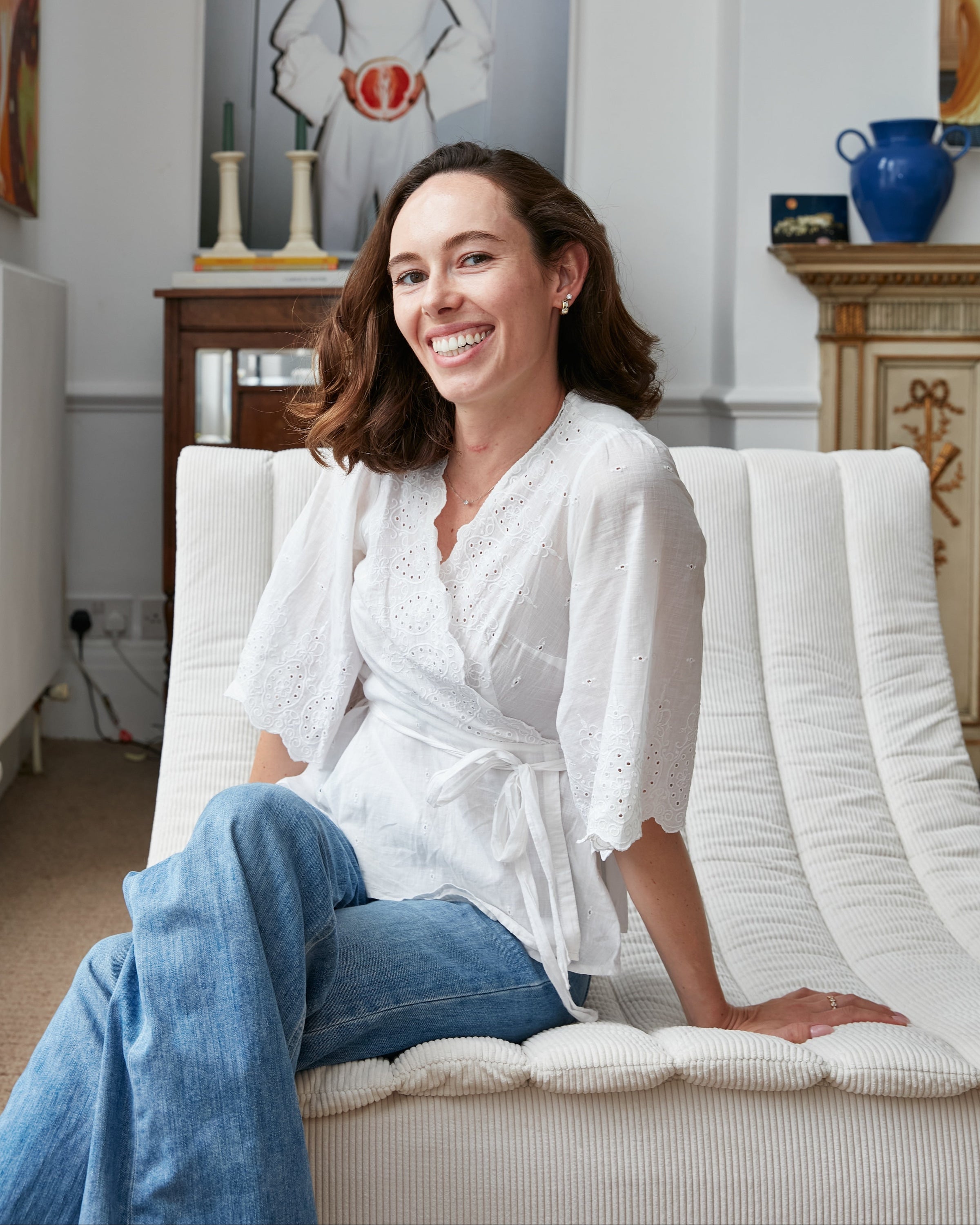 Founder sitting on a white couch wearing a white blouse and blue jeans in a room with decorative items.