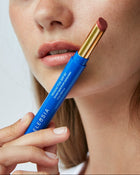 Woman holding a blue lip balm with a gold cap, close-up of the product.