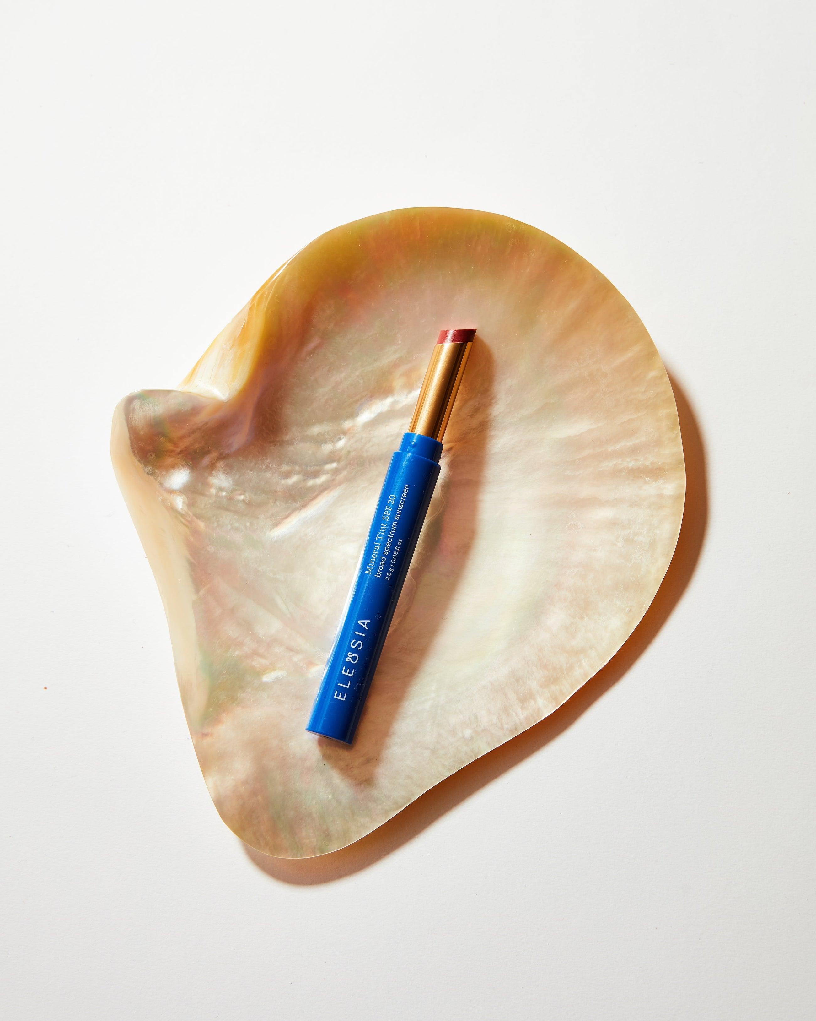 Blue Eleusia lip tint with pink cap on a heart-shaped shell against a white background