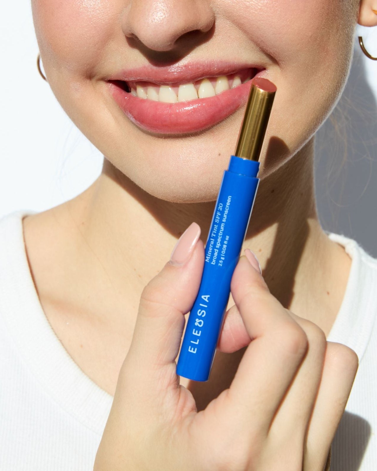ELEUSIA Mineral Lip Tint SPF 20 in Sunny Lotus applied on smiling lips, showing tinted finish and product held near face.